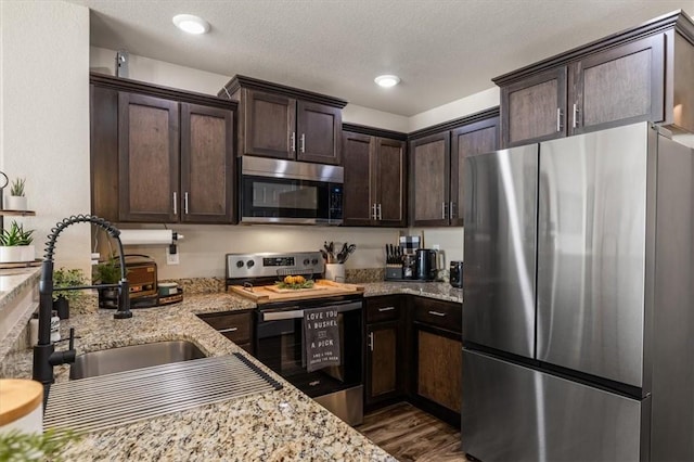 kitchen featuring light stone countertops, appliances with stainless steel finishes, sink, and dark brown cabinetry