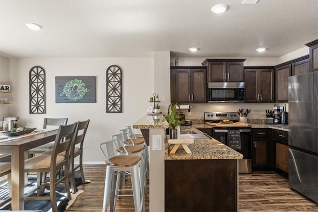 kitchen featuring dark hardwood / wood-style floors, a kitchen bar, dark brown cabinetry, light stone counters, and stainless steel appliances