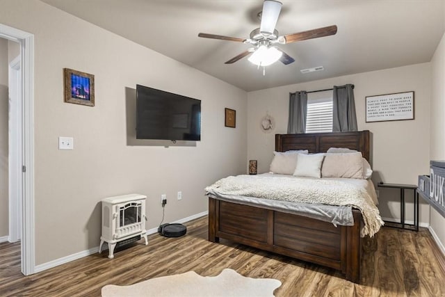 bedroom with ceiling fan, wood-type flooring, and a wood stove