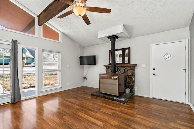 living room featuring ceiling fan, lofted ceiling with beams, a textured ceiling, dark hardwood / wood-style flooring, and a wood stove