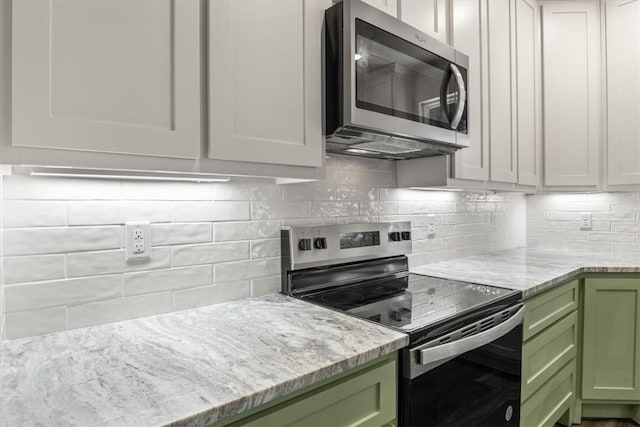 kitchen featuring appliances with stainless steel finishes, backsplash, light stone counters, and green cabinetry