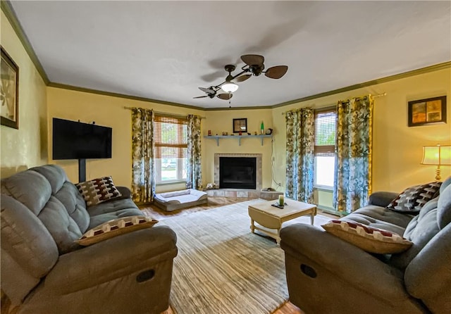 living room with ceiling fan, ornamental molding, a tiled fireplace, and hardwood / wood-style floors