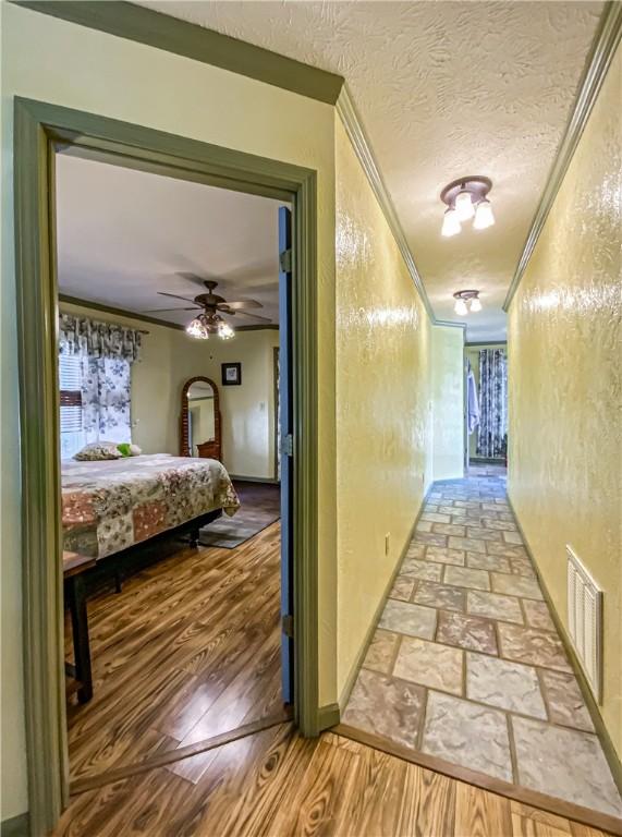 hallway featuring crown molding, a textured ceiling, and light hardwood / wood-style flooring