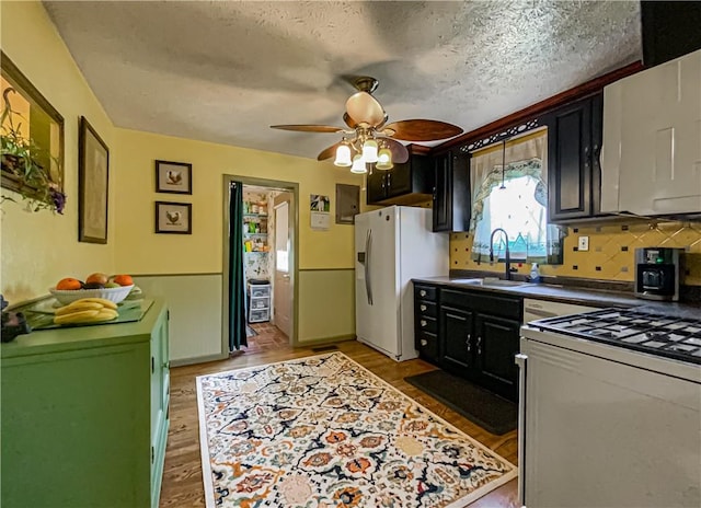 kitchen featuring sink, hardwood / wood-style flooring, white appliances, ceiling fan, and a textured ceiling