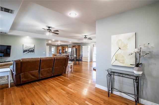 living room featuring hardwood / wood-style flooring, a raised ceiling, plenty of natural light, and ceiling fan