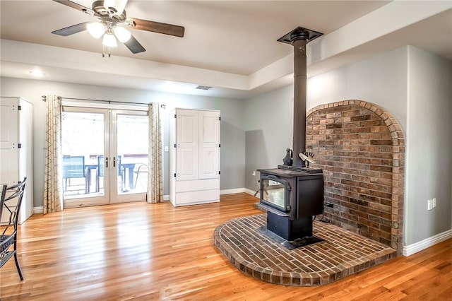 living room with french doors, ceiling fan, light hardwood / wood-style floors, and a wood stove