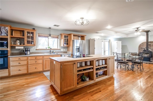 kitchen featuring a kitchen island, decorative light fixtures, sink, a wood stove, and black appliances