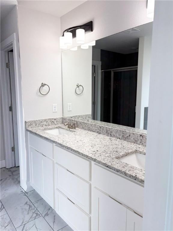 full bathroom with marble finish floor, a sink, double vanity, and a stall shower