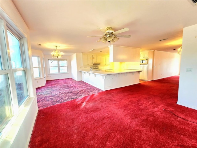 unfurnished living room featuring ceiling fan with notable chandelier and dark colored carpet