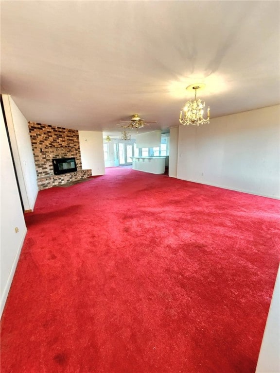 unfurnished living room with a stone fireplace, carpet floors, and ceiling fan with notable chandelier