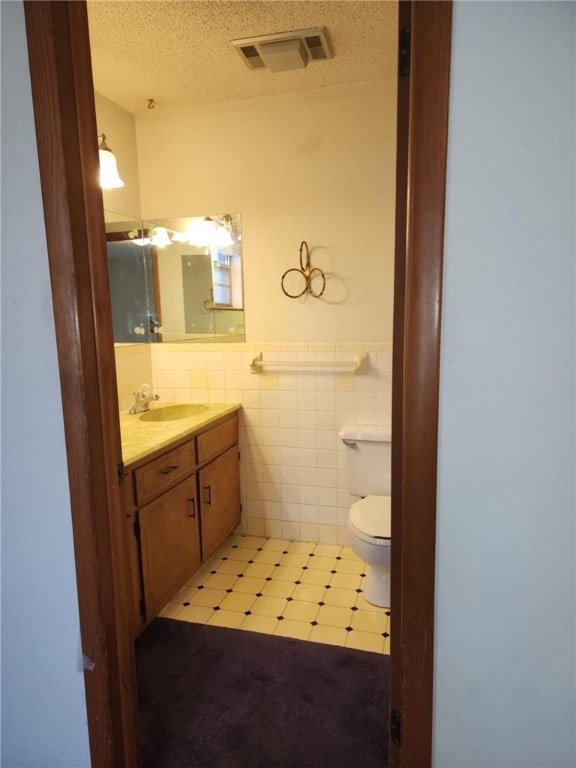 bathroom with tile walls, vanity, toilet, and a textured ceiling