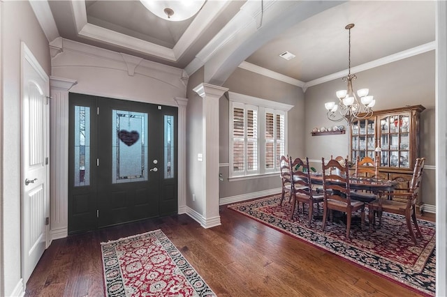 foyer entrance featuring dark wood-type flooring, ornamental molding, a tray ceiling, and ornate columns