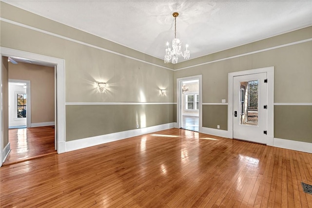 unfurnished room featuring a healthy amount of sunlight, wood-type flooring, and a notable chandelier