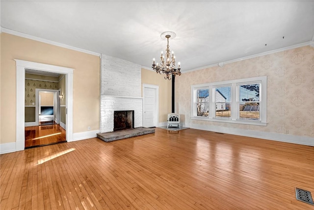 unfurnished living room with an inviting chandelier, crown molding, hardwood / wood-style floors, and a fireplace