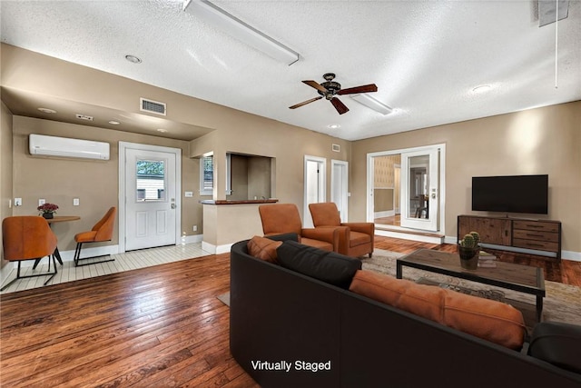 living room with wood-type flooring, a wall mounted air conditioner, a textured ceiling, and ceiling fan