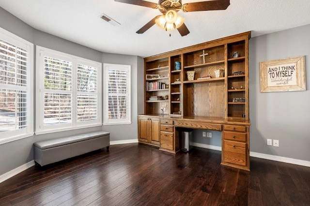 unfurnished office featuring dark wood-type flooring, ceiling fan, and built in desk