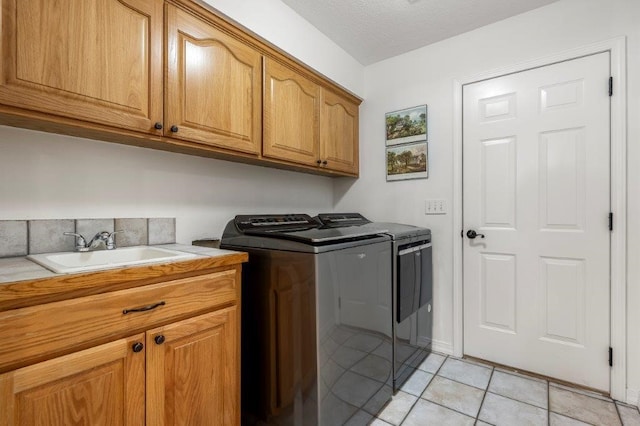 clothes washing area with washing machine and clothes dryer, sink, cabinets, a textured ceiling, and light tile patterned floors