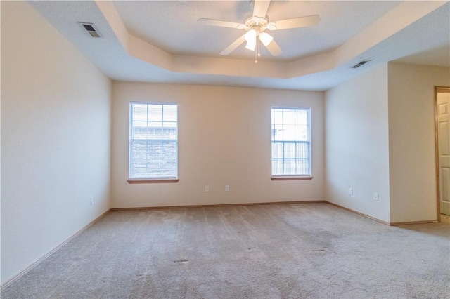 empty room featuring light carpet, a tray ceiling, and ceiling fan