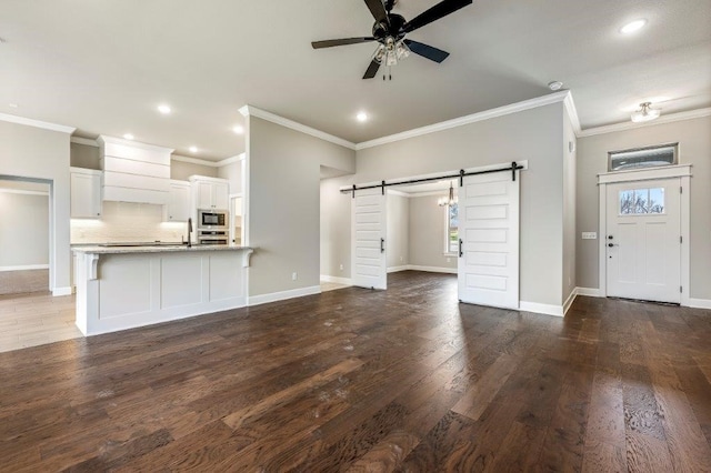 unfurnished living room featuring crown molding, a barn door, wood finished floors, baseboards, and ceiling fan