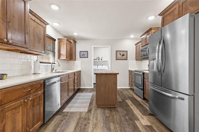 kitchen featuring sink, dark hardwood / wood-style flooring, stainless steel appliances, washing machine and dryer, and backsplash