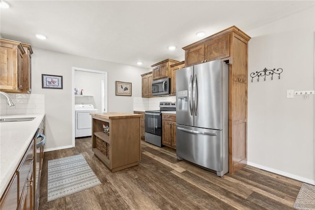 kitchen with dark wood-type flooring, washer / dryer, sink, appliances with stainless steel finishes, and backsplash