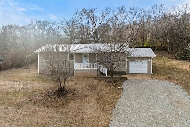 single story home with metal roof, an attached garage, and gravel driveway