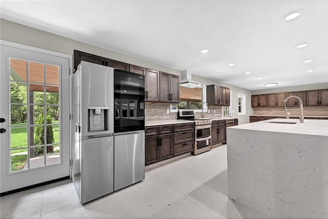 kitchen with sink, backsplash, stainless steel appliances, dark brown cabinets, and wall chimney range hood