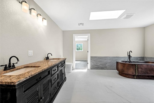 bathroom featuring vanity, a skylight, a tub, and toilet