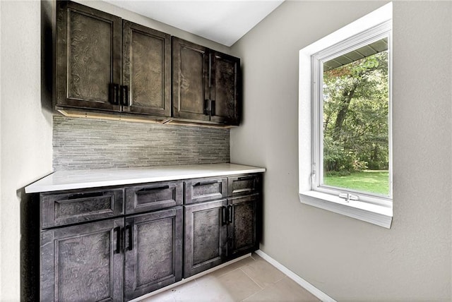 bar with dark brown cabinetry, decorative backsplash, and light tile patterned floors