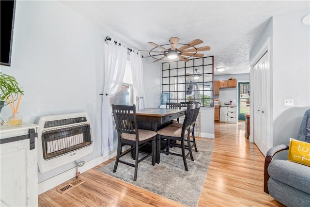 dining area with ceiling fan, a textured ceiling, heating unit, and light wood-type flooring