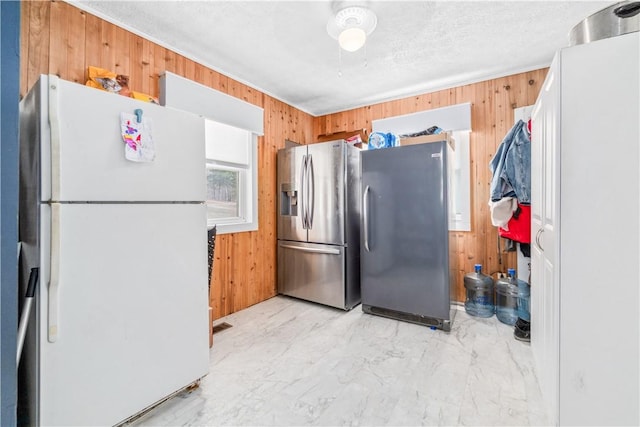 kitchen featuring white refrigerator, stainless steel fridge, a textured ceiling, and wood walls