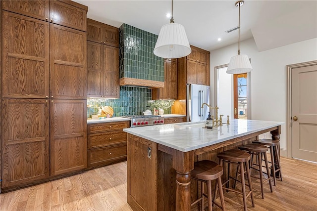 kitchen with decorative light fixtures, decorative backsplash, stainless steel appliances, a center island with sink, and light wood-type flooring