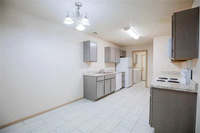 kitchen with sink, gray cabinetry, separate washer and dryer, hanging light fixtures, and white appliances