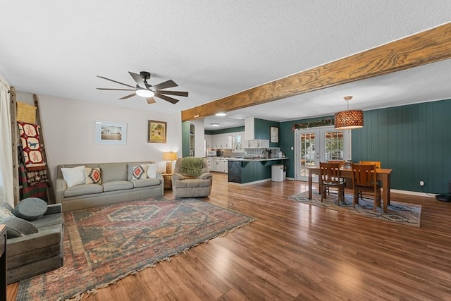 living room featuring ceiling fan, wood-type flooring, a textured ceiling, french doors, and beamed ceiling