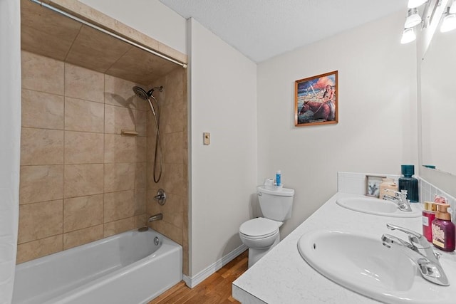 full bathroom featuring tiled shower / bath, wood-type flooring, vanity, toilet, and a textured ceiling