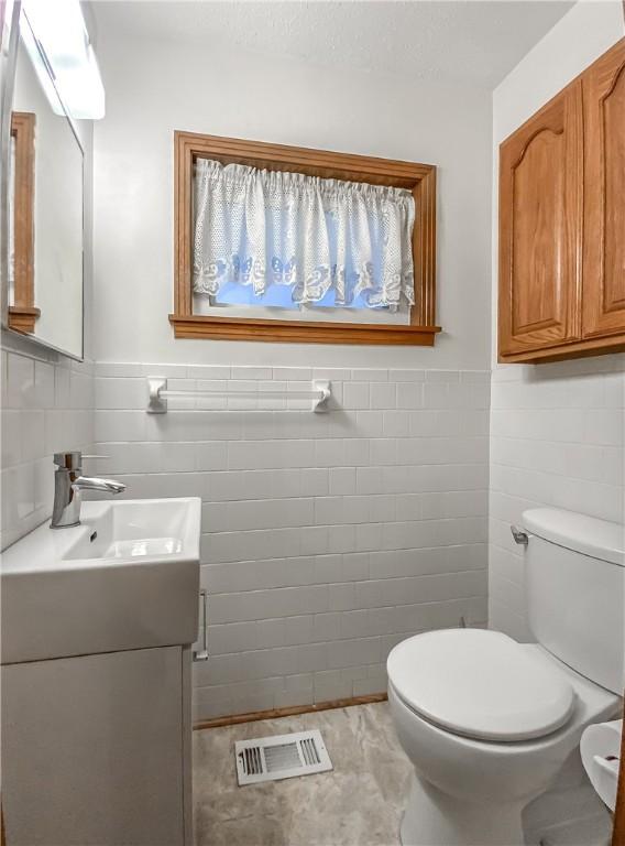 bathroom featuring vanity, tile walls, and toilet