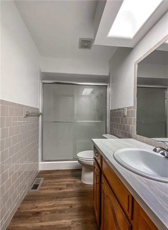 bathroom featuring tile walls, hardwood / wood-style floors, vanity, a shower with shower door, and toilet