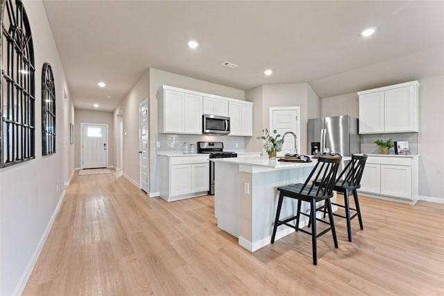 kitchen with appliances with stainless steel finishes, a kitchen breakfast bar, white cabinets, a center island with sink, and light wood-type flooring