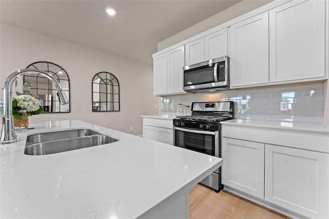 kitchen with sink, stainless steel appliances, tasteful backsplash, light hardwood / wood-style floors, and white cabinets