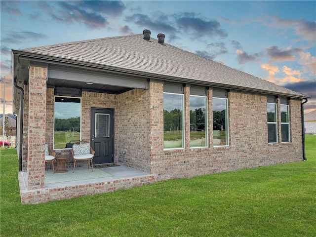 back house at dusk featuring a yard and a patio area