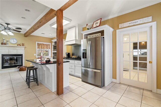 kitchen with premium range hood, appliances with stainless steel finishes, white cabinetry, a kitchen breakfast bar, and light tile patterned floors