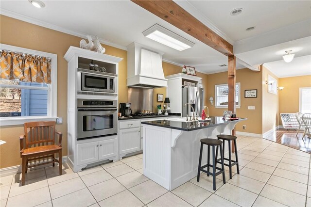 kitchen with a breakfast bar, a center island with sink, custom range hood, stainless steel appliances, and white cabinets