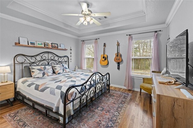 bedroom with multiple windows, a tray ceiling, wood-type flooring, and ornamental molding