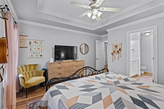 bedroom with crown molding, ensuite bath, ceiling fan, a tray ceiling, and light hardwood / wood-style floors