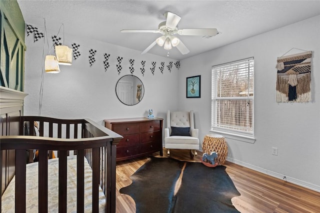 bedroom with a textured ceiling, light hardwood / wood-style floors, a nursery area, and ceiling fan