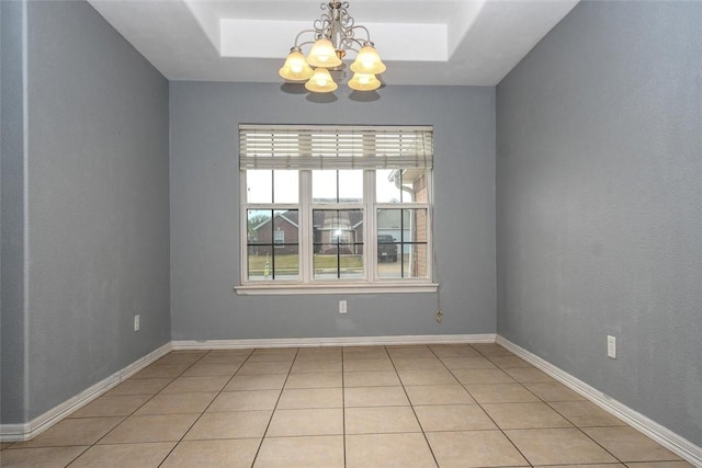 empty room with a tray ceiling, a chandelier, and light tile patterned floors