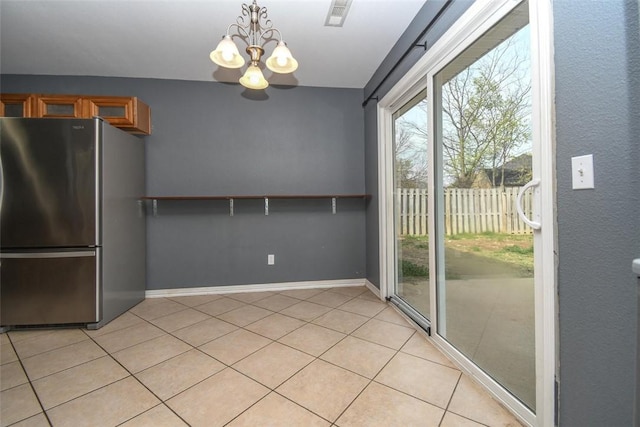 interior space featuring an inviting chandelier, baseboards, light tile patterned flooring, freestanding refrigerator, and brown cabinetry