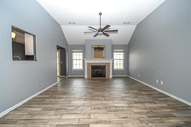 unfurnished living room with baseboards, ceiling fan, a tiled fireplace, and a wealth of natural light
