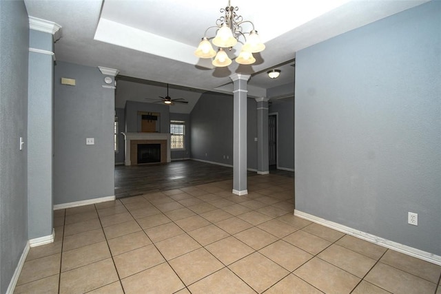 unfurnished living room featuring ornate columns, light tile patterned floors, baseboards, and ceiling fan with notable chandelier