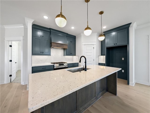 kitchen featuring sink, custom exhaust hood, light stone counters, decorative light fixtures, and an island with sink